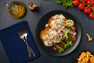 Kızarmış morina, patatesli krep, mantar sosu ve salata ile servis edilir. Siyah bir tabakta porsiyon. Koyu arkaplan.