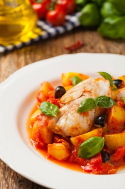 Geleneksel ispanyolca morina balığı. Domates sosunda haşlanmış patates, olivki ve fesleğen ile servis edilmiş. Ön görünüm. 