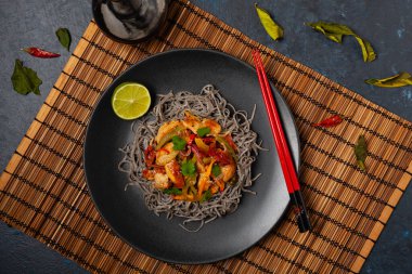 Siyah susamlı buğday eriştesi, tavuk ve sebzeli tavada kızartılmış. Üst Manzara. Siyah bir tabakta servis edildi..