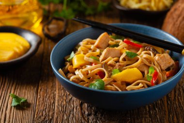 Mangolu kızarmış tavuk ve erişteli hindistan cevizi sütü. Bir tavada hazır. Ön manzara. Mavi bir kasede servis edildi..