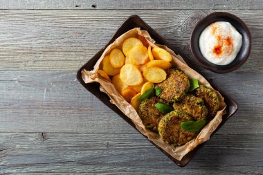 Vejetaryen ıspanak ve brokoli köftesi, yoğurt sosu ve kızarmış patatesle servis ediliyor. Üst görünüm.