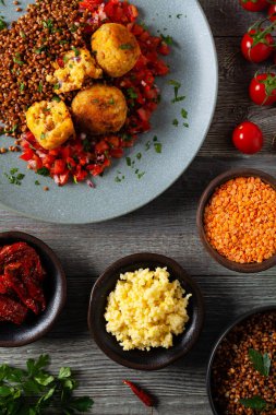 Mercimek ve darı köftesi. Karabuğdaylı domates sosu ile servis edilmiş. Gri plaka, arka planda tahta tahtalar. Üst görünüm.