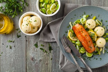 Bir porsiyon kızarmış somon, patates püresi ve pişmiş pırasa ile servis edilir. Üst Manzara. Gri plaka, ahşap arka plan. 