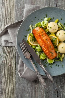 Bir porsiyon kızarmış somon, patates püresi ve pişmiş pırasa ile servis edilir. Üst Manzara. Gri plaka, ahşap arka plan. 