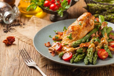 Kızarmış tavuk göğsü, kuşkonmazla servis edilen domates sosu, kurutulmuş domates. Ön görünüm.