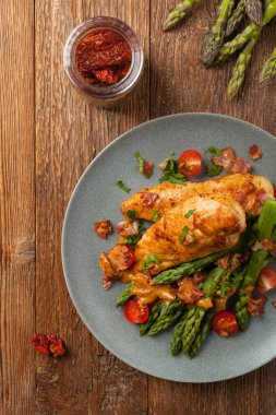 Kızarmış tavuk göğsü, kuşkonmazla servis edilen domates sosu, kurutulmuş domates. Üst görünüm.