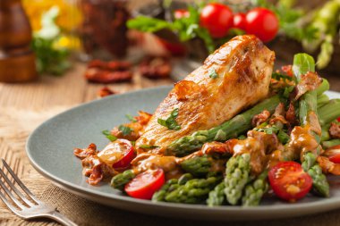 Kızarmış tavuk göğsü, kuşkonmazla servis edilen domates sosu, kurutulmuş domates. Ön görünüm.