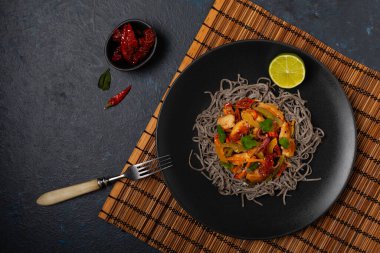 Siyah susamlı buğday eriştesi, tavuk ve sebzeli tavada kızartılmış. Üst Manzara. Siyah bir tabakta servis edildi..