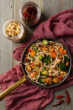 Tavuk, brokoli ve havuçla karıştırılmış makarna. Üst Manzara. Gri ahşap arka plan. Kızartma tavasında servis edilir..