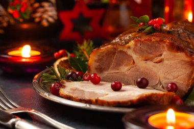 Noel tarzında kızarmış domuz boynu. Koyu lacivert arka plan. Noel aksesuarları. Arka planda mumlar ve fenerler..