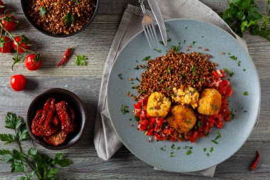 Mercimek ve darı köftesi. Karabuğdaylı domates sosu ile servis edilmiş. Gri plaka, arka planda tahta tahtalar. Üst görünüm.
