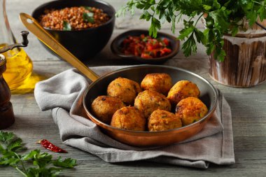 Mercimek ve darı köftesi. Karabuğdaylı domates sosu ile servis edilmiş. Gri plaka, arka planda tahta tahtalar. Ön görünüm.