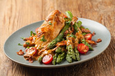 Kızarmış tavuk göğsü, kuşkonmazla servis edilen domates sosu, kurutulmuş domates. Ön görünüm.