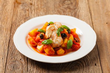 Geleneksel ispanyolca morina balığı. Domates sosunda haşlanmış patates, olivki ve fesleğen ile servis edilmiş. Ön görünüm. 