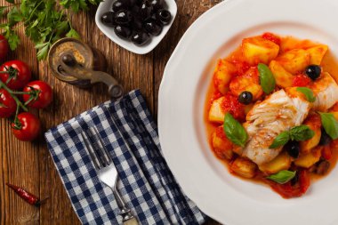 Geleneksel ispanyolca morina balığı. Domates sosunda haşlanmış patates, olivki ve fesleğen ile servis edilmiş. Üst görünüm. 