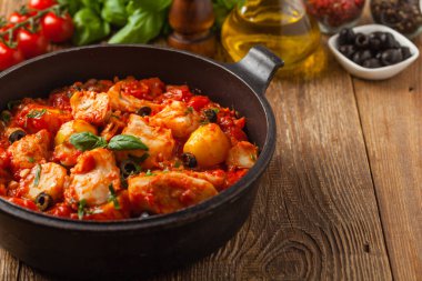 Geleneksel ispanyolca morina balığı. Domates sosunda haşlanmış patates, olivki ve fesleğen ile servis edilmiş. Ön görünüm. 