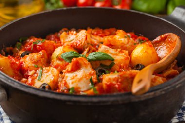 Geleneksel ispanyolca morina balığı. Domates sosunda haşlanmış patates, olivki ve fesleğen ile servis edilmiş. Ön görünüm. 