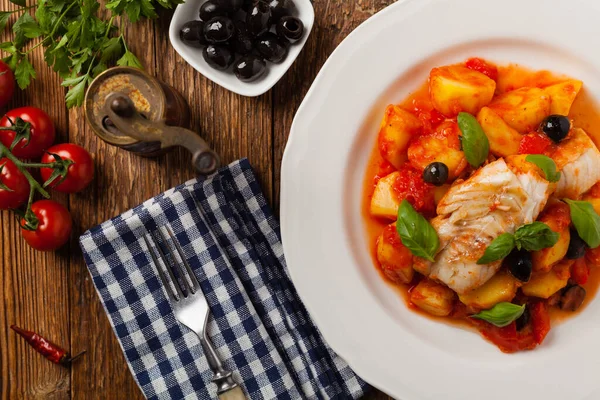 Geleneksel ispanyolca morina balığı. Domates sosunda haşlanmış patates, olivki ve fesleğen ile servis edilmiş. Üst görünüm. 