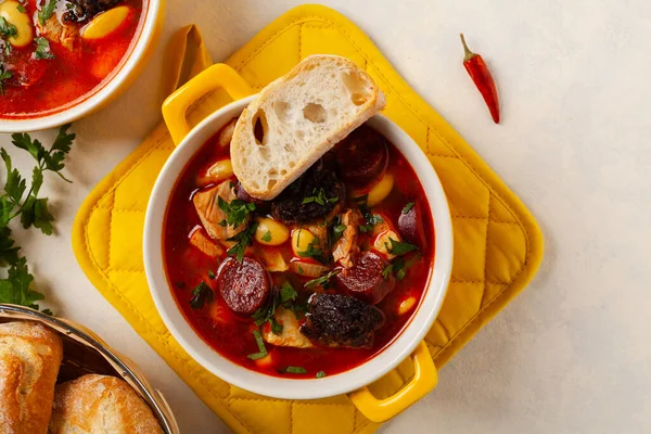 Geleneksel İspanyol gulaş çorbası. Fabada Asturiana. Kapaklı sarı kilden bir çömlekle servis edilmiş. Üst görünüm.