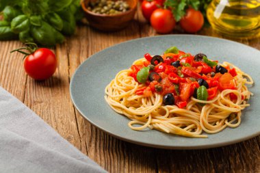 Domates ve zeytinli İtalyan spagetti alla Pultanesca. Et ve peynir olmadan servis edilir. Ön manzara. Doğal ahşap zemin. 