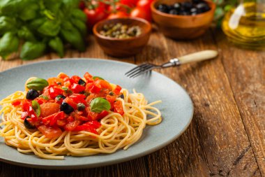 Domates ve zeytinli İtalyan spagetti alla Pultanesca. Et ve peynir olmadan servis edilir. Ön manzara. Doğal ahşap zemin. 