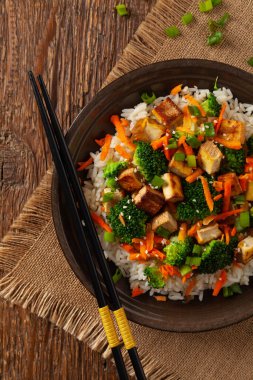 Pilav ve sebzeli soya peyniri. Kahverengi tabakta yemek çubuklarıyla servis ediliyor. Üst görünüm.