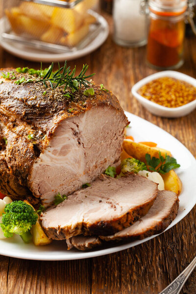 Whole cooked pork neck. Served on a white plate with vegetables and baked potatoes.