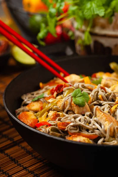 Wheat noodles with black sesame, fried in a wok with chicken and vegetables. Front view.