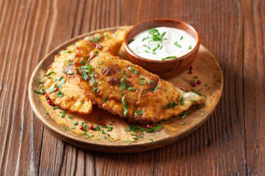 Geleneksel cheebureki, ahşap bir tabakta sos ile servis edilir. Maydanozla süslenmiş..