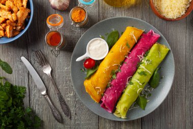 Tavuk ve vejetaryen dolgulu renkli krepler. Doğal olarak meyve suyu ya da baharatla renklendirilmiş. Sos ya da yoğurt ile servis edilir. Ahşap arkaplan.