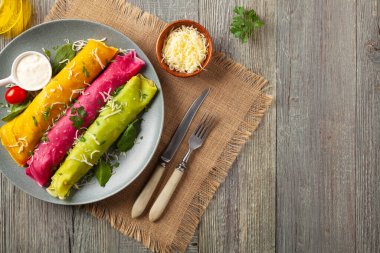 Tavuk ve vejetaryen dolgulu renkli krepler. Doğal olarak meyve suyu ya da baharatla renklendirilmiş. Sos ya da yoğurt ile servis edilir. Ahşap arkaplan.