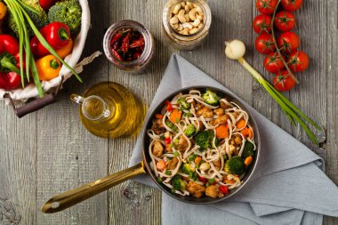 Tavuk, brokoli ve havuçla karıştırılmış makarna. Üst Manzara. Gri ahşap arka plan. Kızartma tavasında servis edilir..