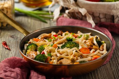 Tavuk, brokoli ve havuçla karıştırılmış makarna. Kızartma tavasında servis edilir..