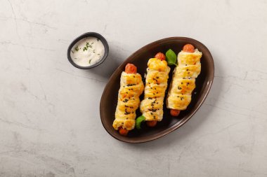 Puf böreğinde pişmiş sosis. Susam tohumları serpilmiş, sosla servis edilmiş. Taş arkaplan.