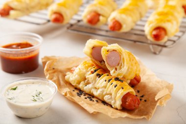 Puf böreğinde pişmiş sosis. Susam tohumları serpilmiş, sosla servis edilmiş. Taş arkaplan.