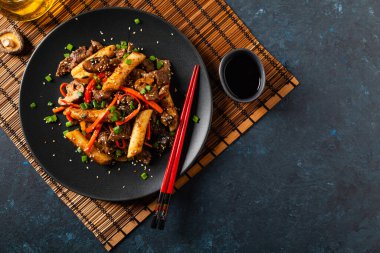Geleneksel Kore Tteokbokki pirinç eriştesi sığır eti, sebze ve kaka mantarı. Bir tavada hazır. Koyu mavi arkaplan. 