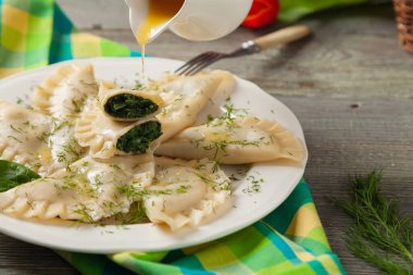 Ispanaklı hamur tatlısı, eritilmiş tereyağı ve doğranmış dereotu serpiştirilmiş. Ahşap arka plan. Beyaz tabak. 