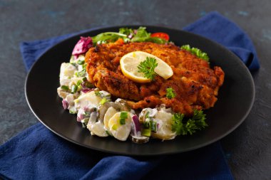 Klasik, geleneksel Viyana sığır filetosu şnitzel. Patates salatasında servis edildi. Üremiş. Koyu arkaplan.