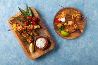 Somon ve ananaslı ızgara şiş kebap. Yoğurt sosuyla servis edilir. Mavi boyalı arkaplan.