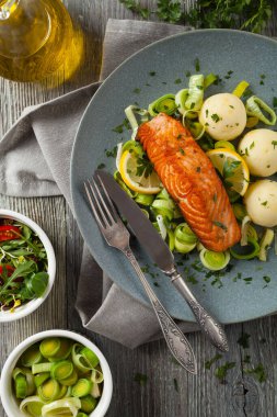 Bir porsiyon kızarmış somon, patates püresi ve pişmiş pırasa ile servis edilir. Üst Manzara. Gri plaka, ahşap arka plan. 