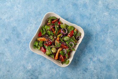 Geniş fasulyeli ve tavuklu lezzetli salata. Mavi boyalı arka planda bir kasede servis edilmiş..