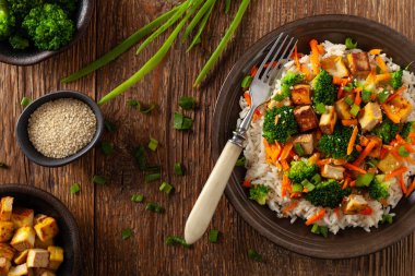 Pilav ve sebzeli soya peyniri. Kahverengi tabakta yemek çubuklarıyla servis ediliyor. Üst görünüm.