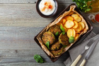 Vejetaryen ıspanak ve brokoli köftesi, yoğurt sosu ve kızarmış patatesle servis ediliyor. Üst görünüm.