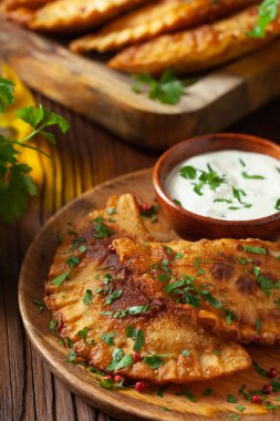 Geleneksel cheebureki, ahşap bir tabakta sos ile servis edilir. Maydanozla süslenmiş..