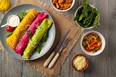 Tavuk ve vejetaryen dolgulu renkli krepler. Doğal olarak meyve suyu ya da baharatla renklendirilmiş. Sos ya da yoğurt ile servis edilir. Ahşap arkaplan.