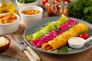 Tavuk ve vejetaryen dolgulu renkli krepler. Doğal olarak meyve suyu ya da baharatla renklendirilmiş. Sos ya da yoğurt ile servis edilir. Ahşap arkaplan.