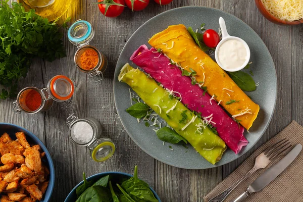 Tavuk ve vejetaryen dolgulu renkli krepler. Doğal olarak meyve suyu ya da baharatla renklendirilmiş. Sos ya da yoğurt ile servis edilir. Ahşap arkaplan.