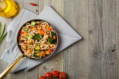 Tavuk, brokoli ve havuçla karıştırılmış makarna. Üst Manzara. Gri ahşap arka plan. Kızartma tavasında servis edilir..