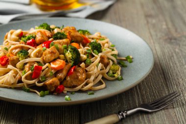 Tavuk, brokoli ve havuçla karıştırılmış makarna. Gri bir tabakta servis edilir..