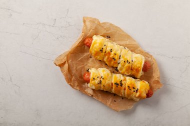 Puf böreğinde pişmiş sosis. Susam tohumları serpilmiş, sosla servis edilmiş. Taş arkaplan.